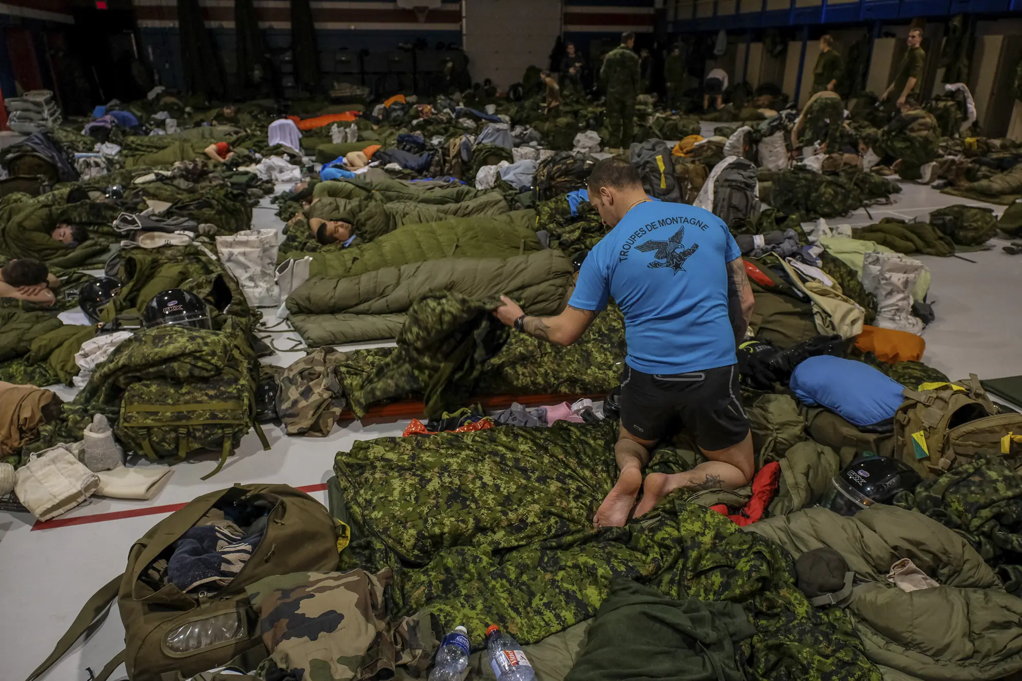 A French mountain soldier arranges kit among dozens sleeping on a gymnasium floor