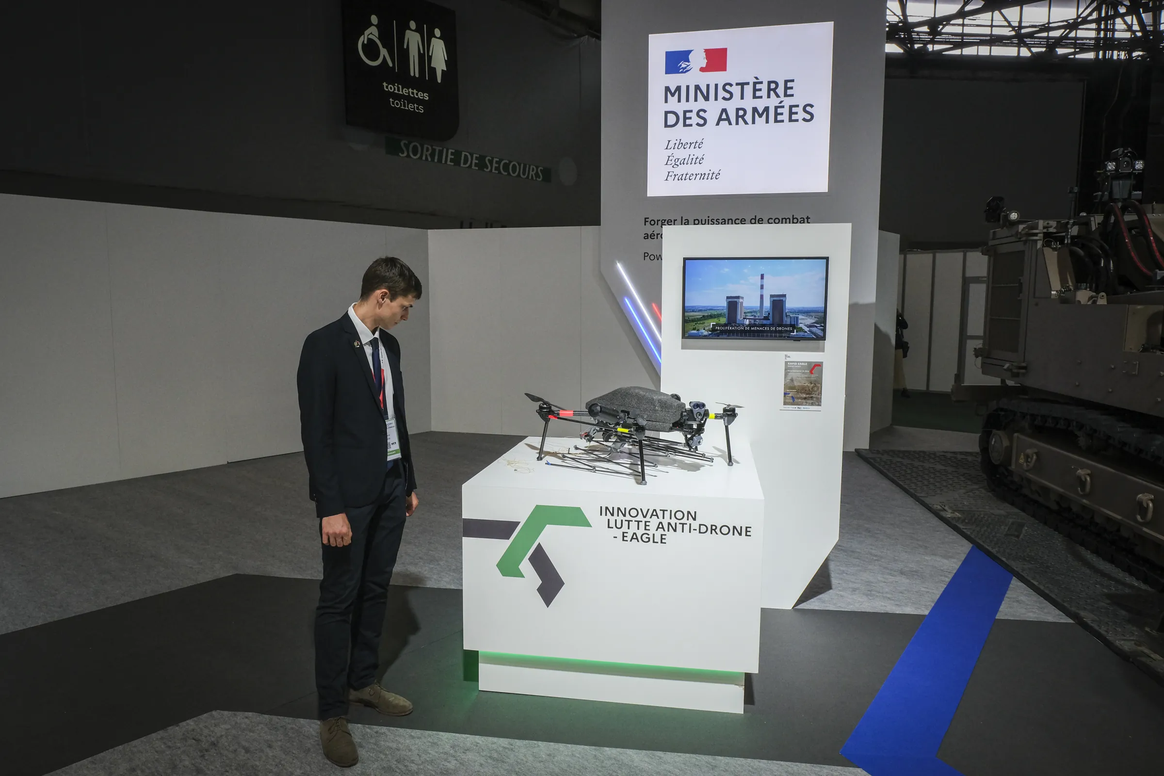 A lone visitor studies a counter-drone quadcopter on a white plinth at the French Ministry of Defence stand
