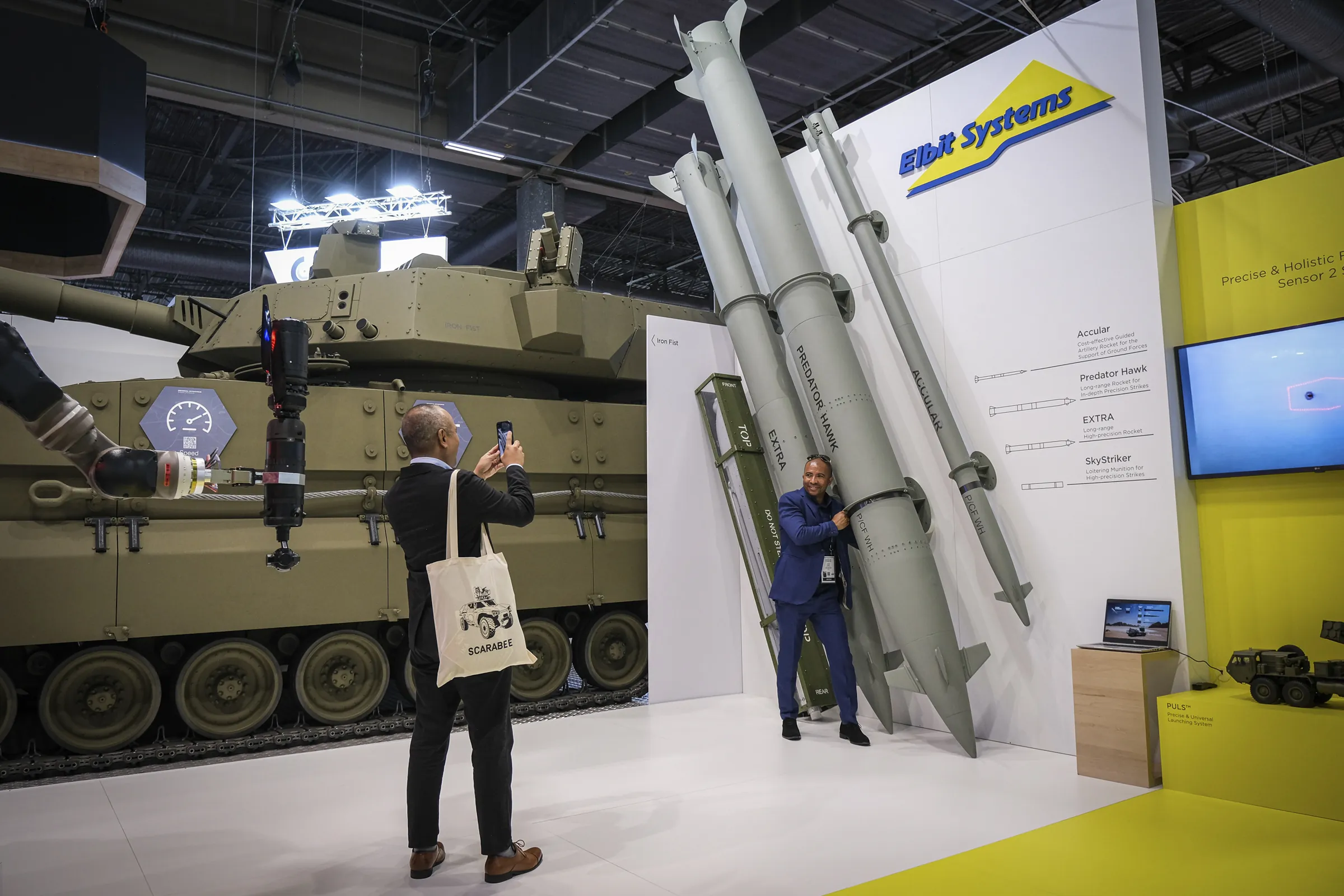 A visitor poses hugging giant display rockets while a friend photographs him