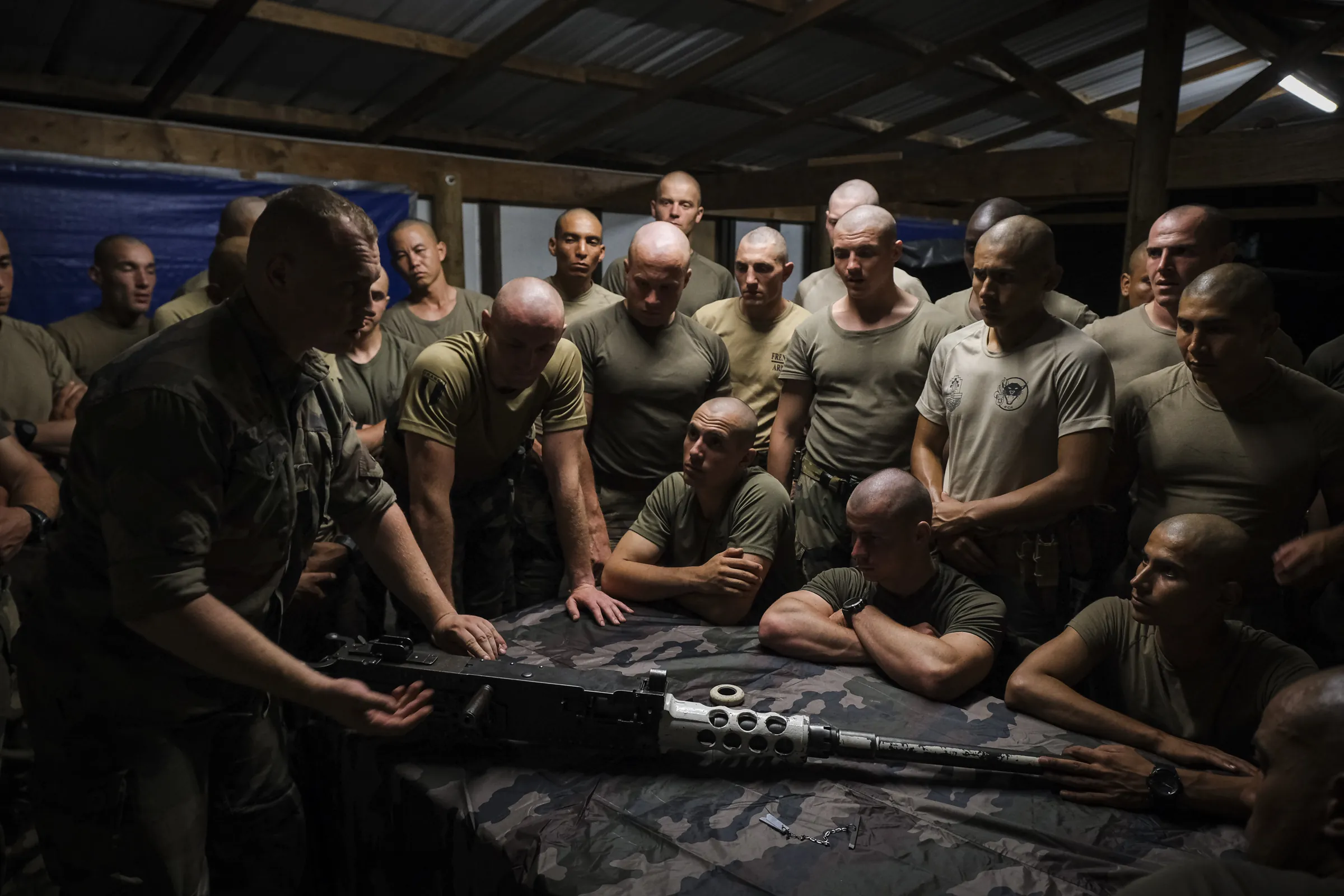 Night weapons lesson under a tin roof: an instructor explains a heavy machine gun to a packed crowd of Foreign Legion recruits