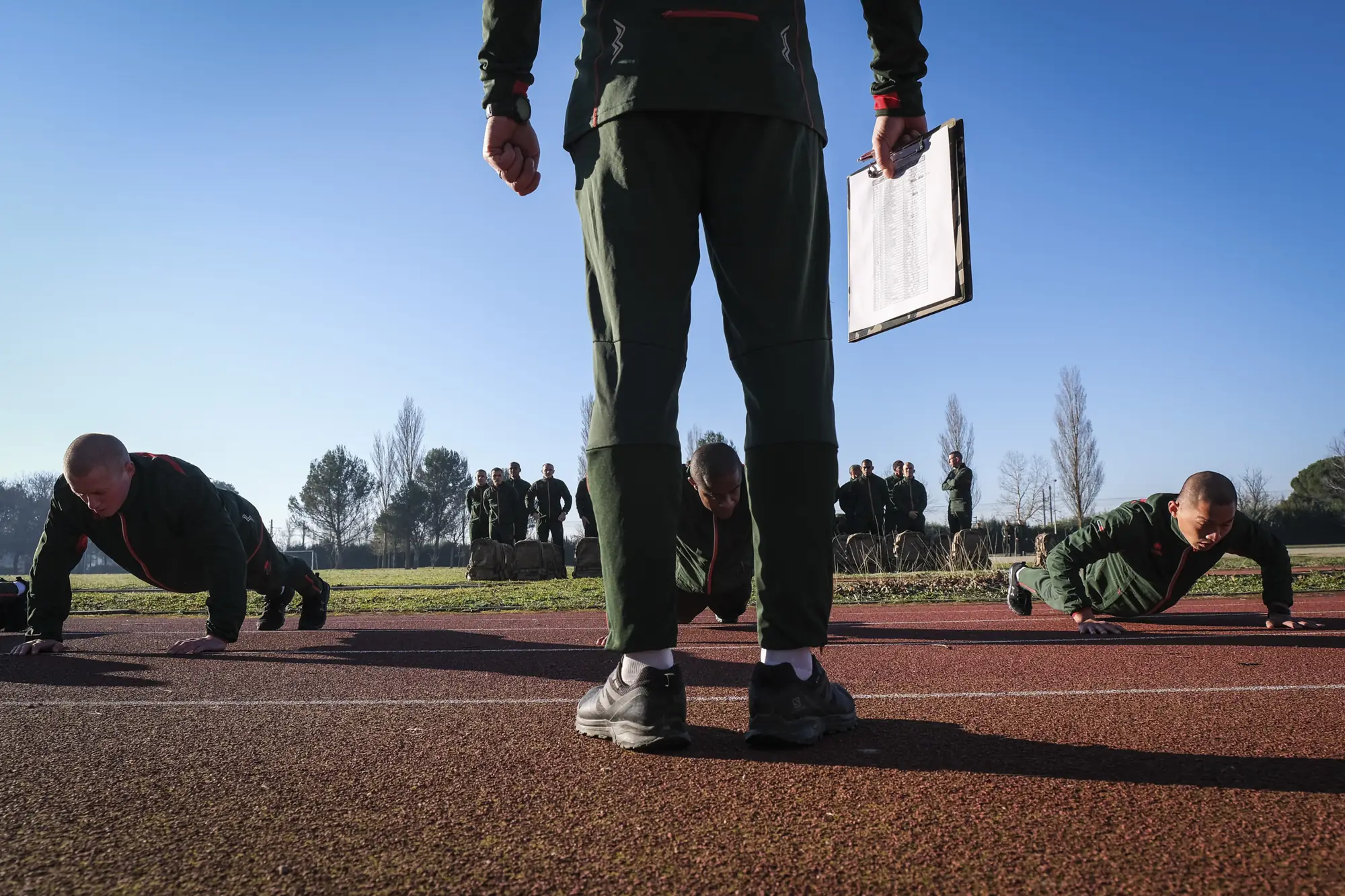 Push-up fitness test on a running track, an instructor with a clipboard in the foreground