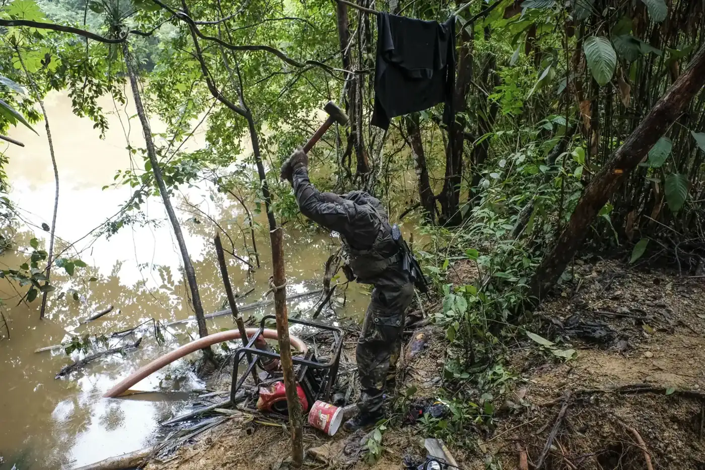 A French soldier destroys a seized motor-pump with a sledgehammer on a riverbank in French Guiana