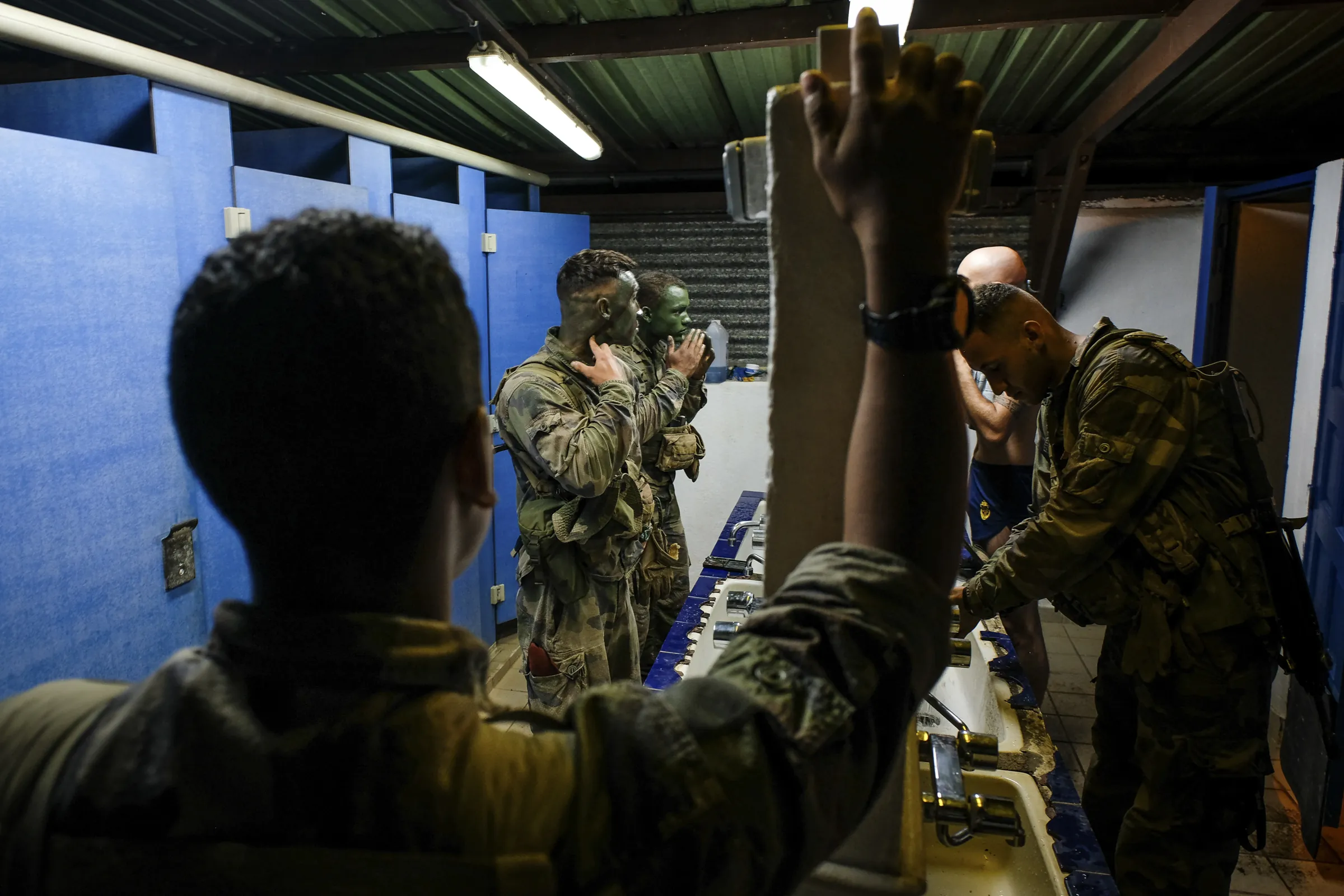 French soldiers apply camouflage face paint at barracks sinks before dawn, French Guiana