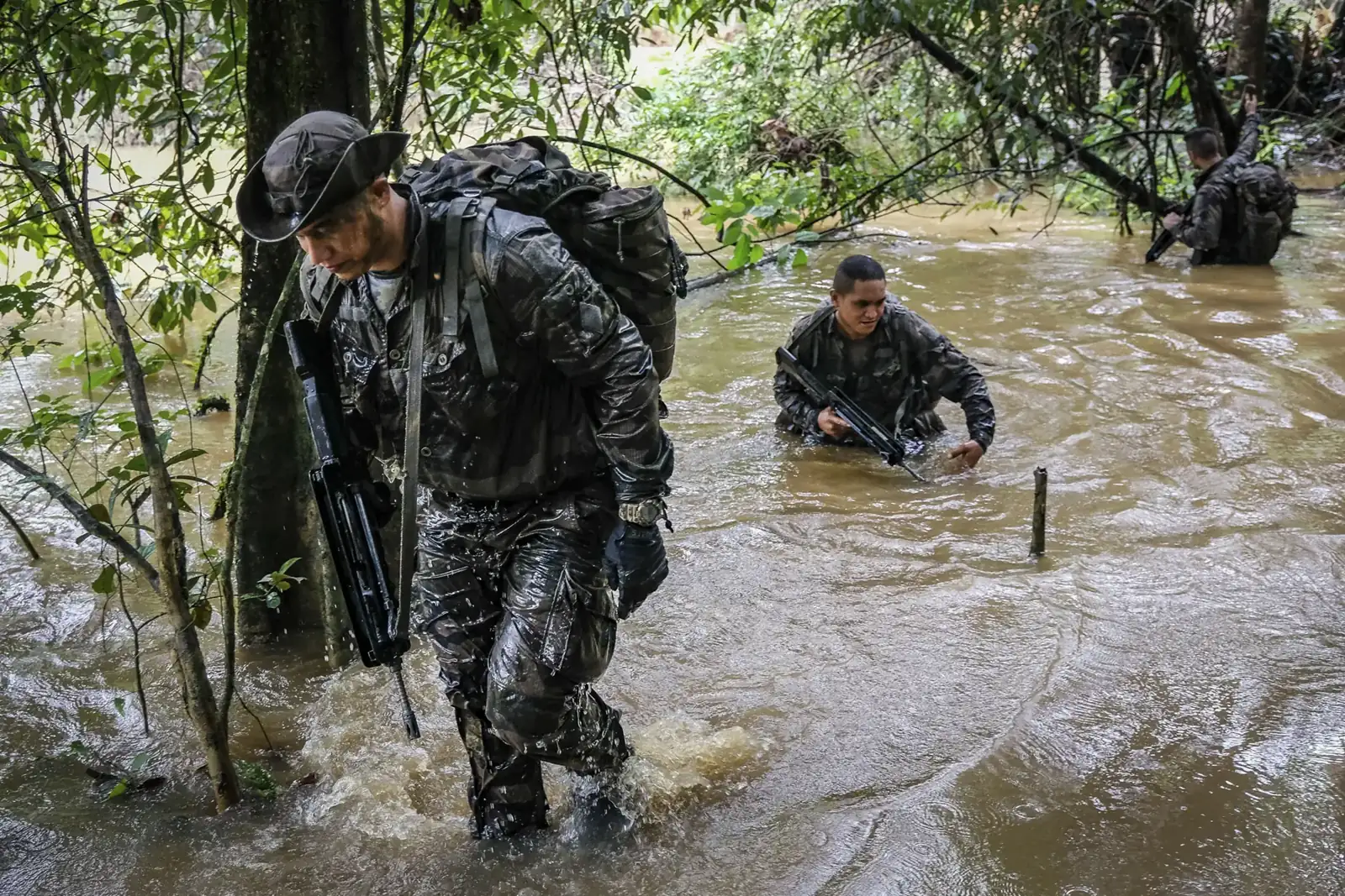 Three French soldiers wade chest-deep through a flooded creek carrying their rifles, French Guiana