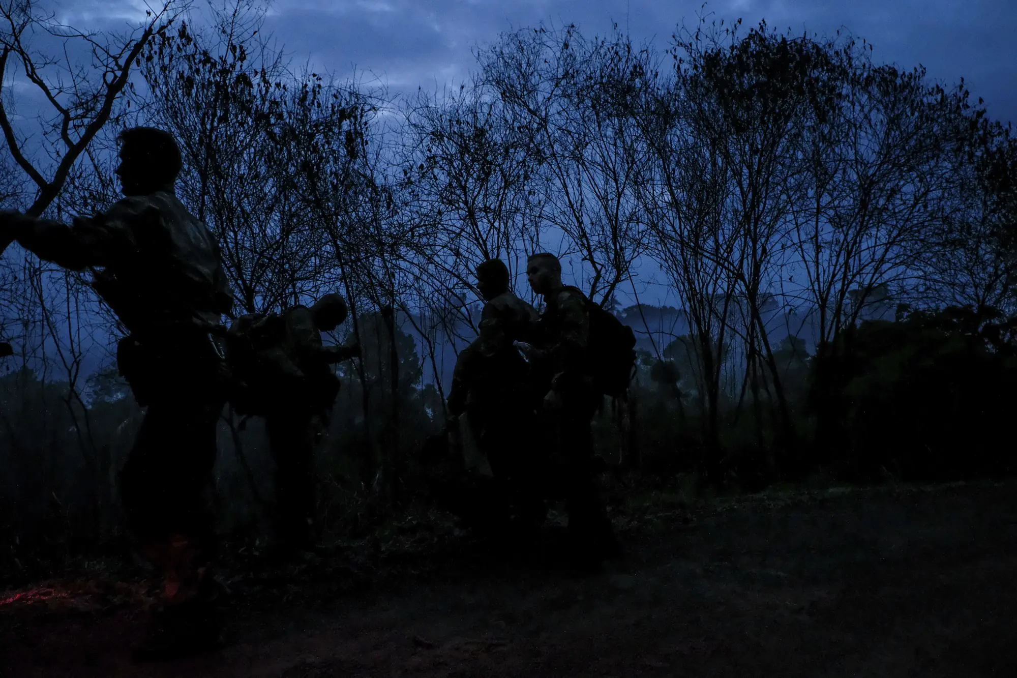 A silhouetted French patrol column moves through scrub at dusk in French Guiana