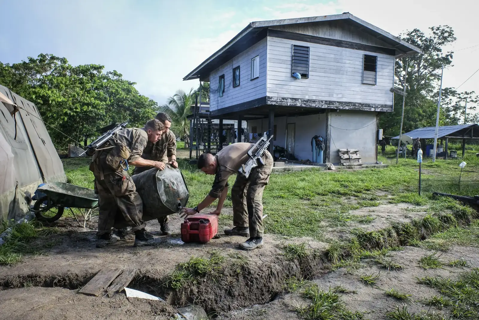 French soldiers decant fuel into a jerrycan beside a stilt house at a forward base