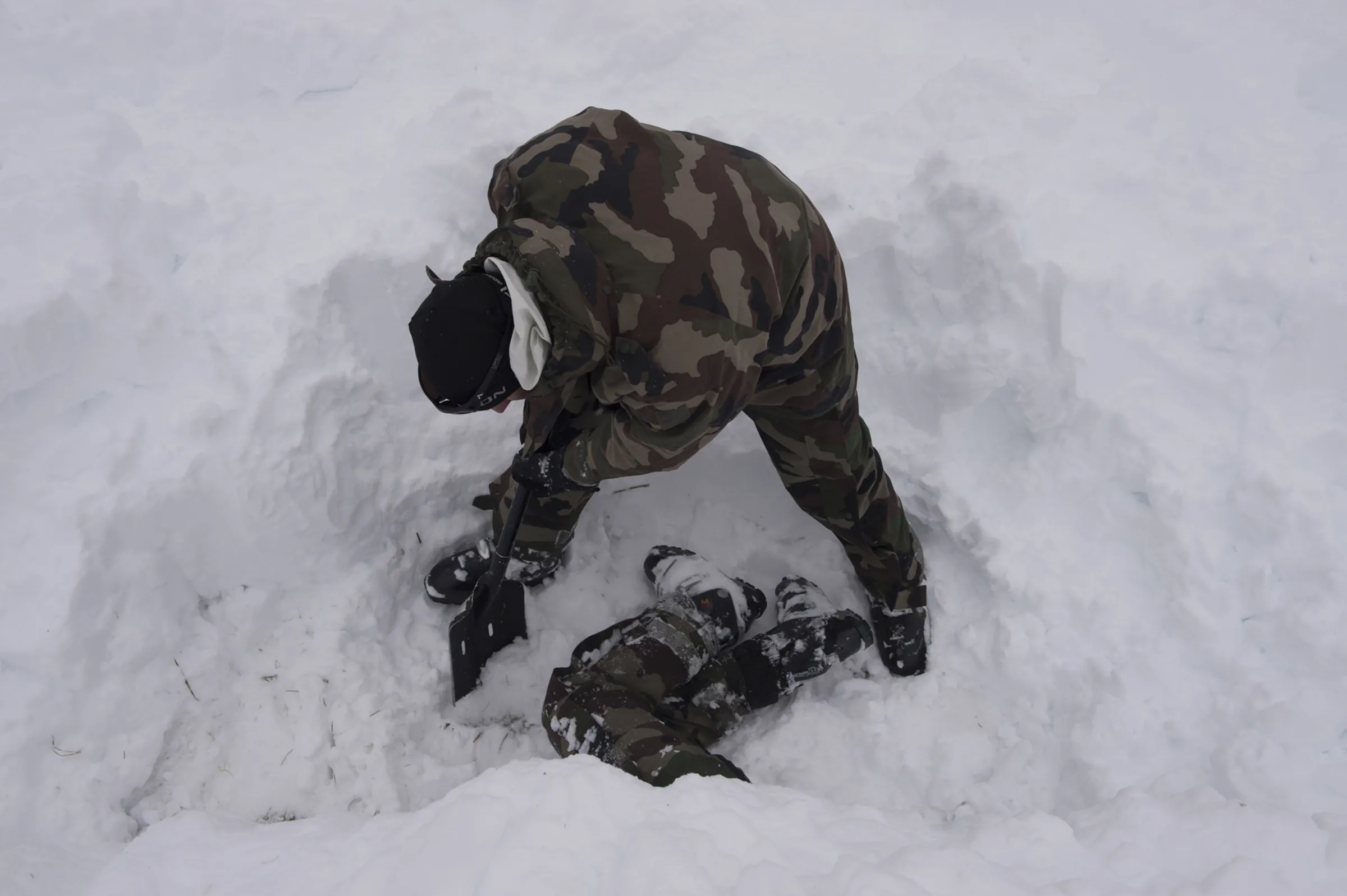 A mountain soldier shovels snow while building an igloo during survival training