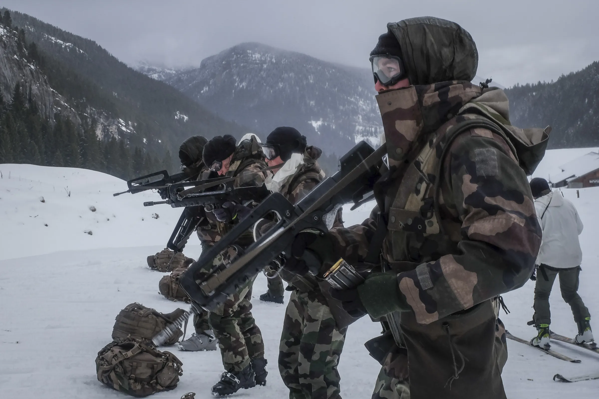 A squad of French soldiers readies rifles in a snowy valley beneath grey cliffs