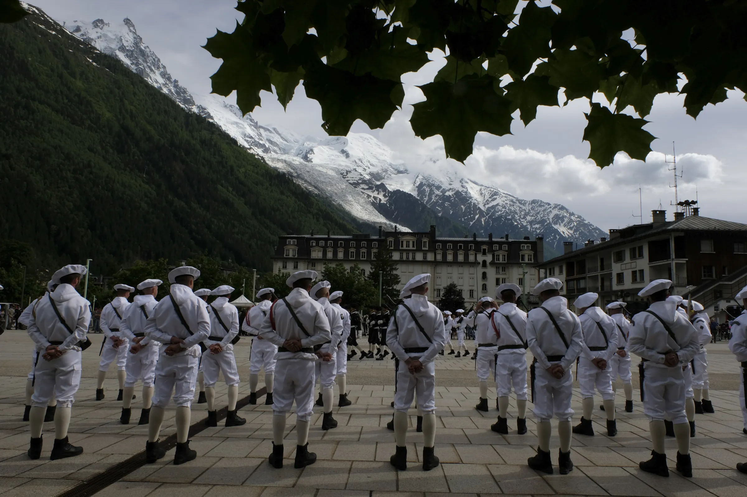 Mountain troops in white parade uniform on a Chamonix square, Mont Blanc massif towering behind