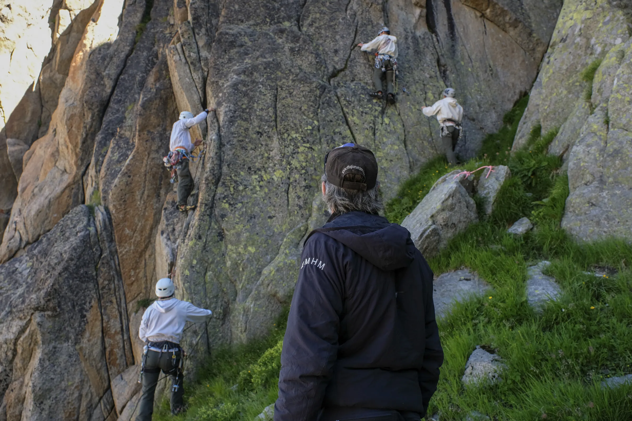An instructor watches four trainees climbing a granite crag in soft evening light