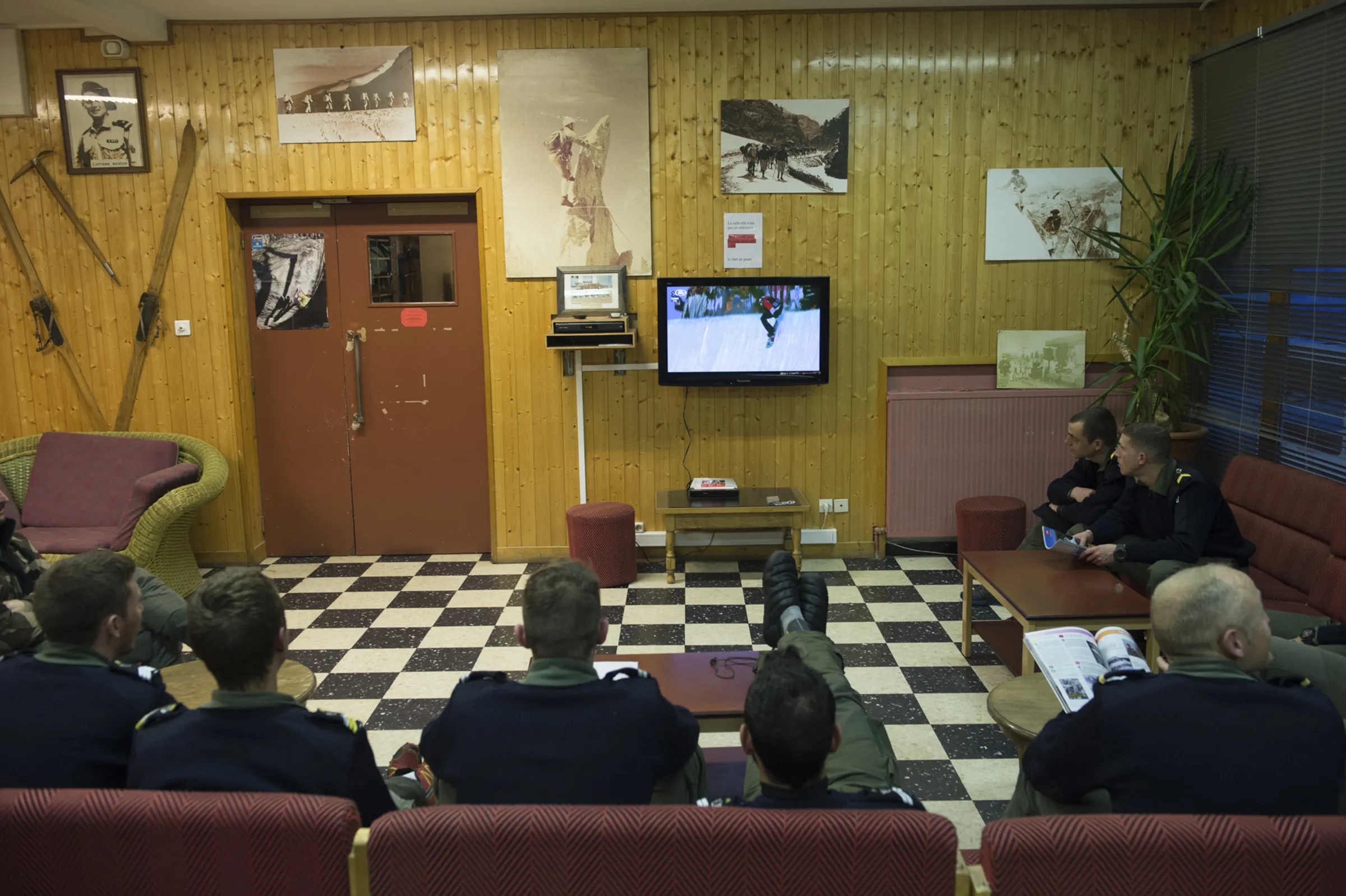 Soldiers take a break in an Alpine hunters’ cabin, vintage skis and ice axes on the walls