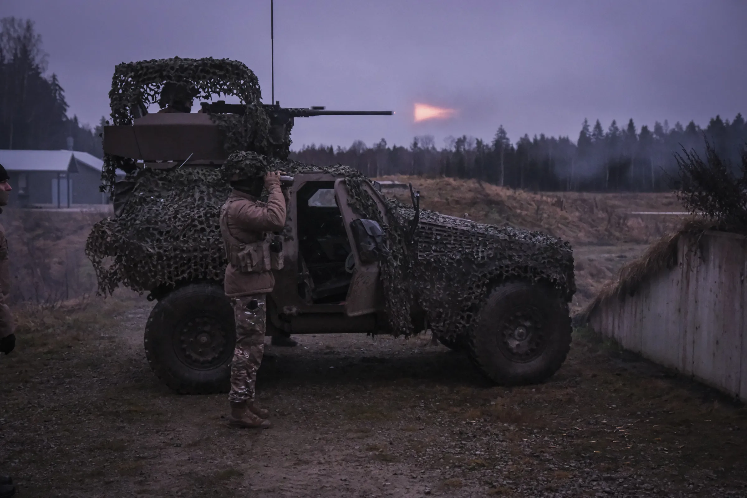 A camouflage-netted French recon vehicle fires its heavy machine gun at dusk