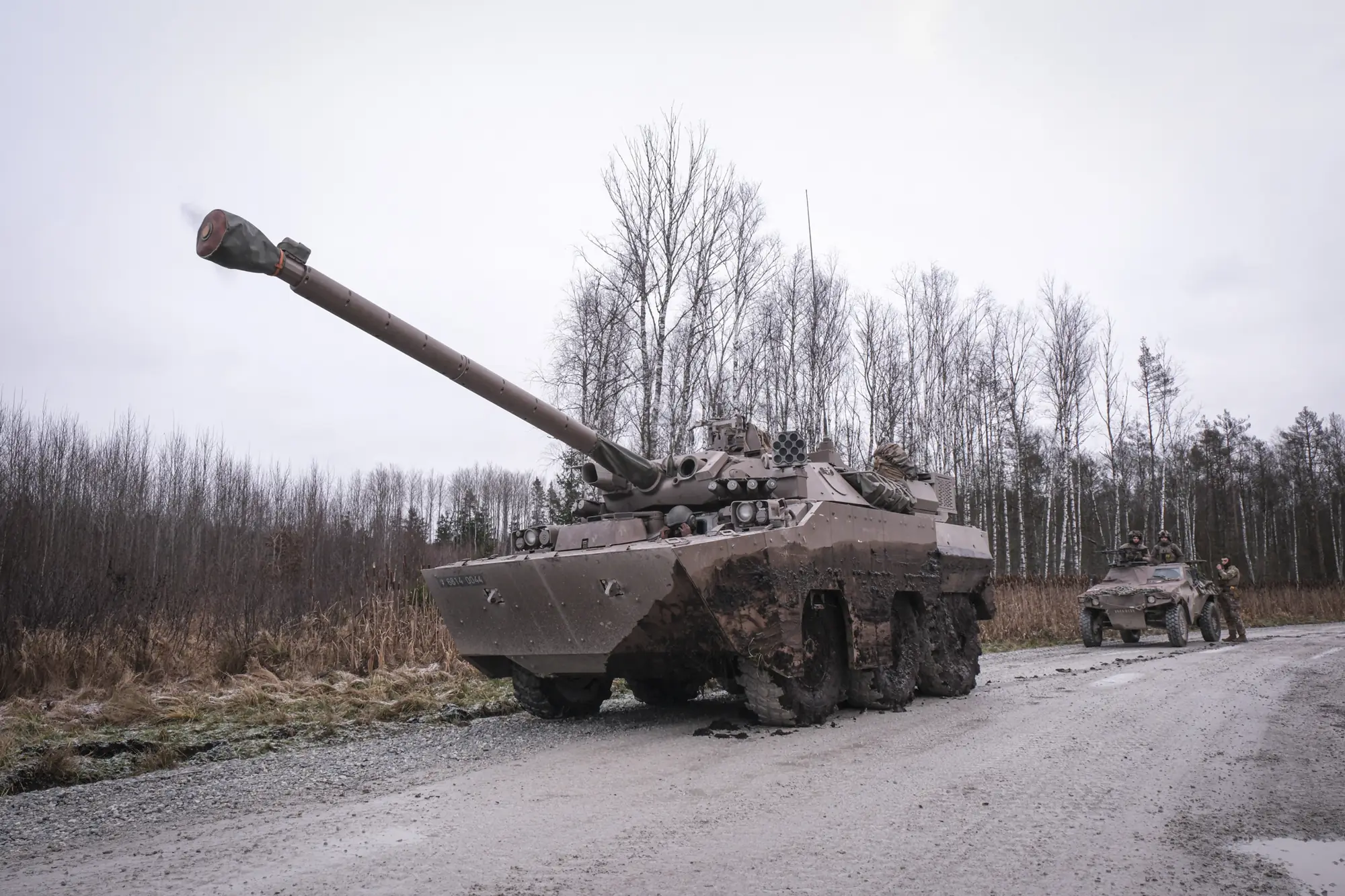 A mud-caked French AMX-10 RC armoured vehicle on a gravel road among bare birches