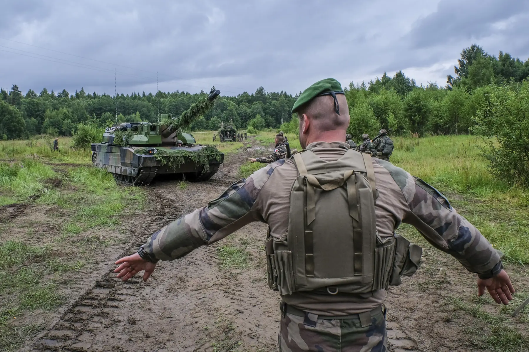 A green-bereted Legion NCO guides a spruce-camouflaged Leclerc tank on a muddy track
