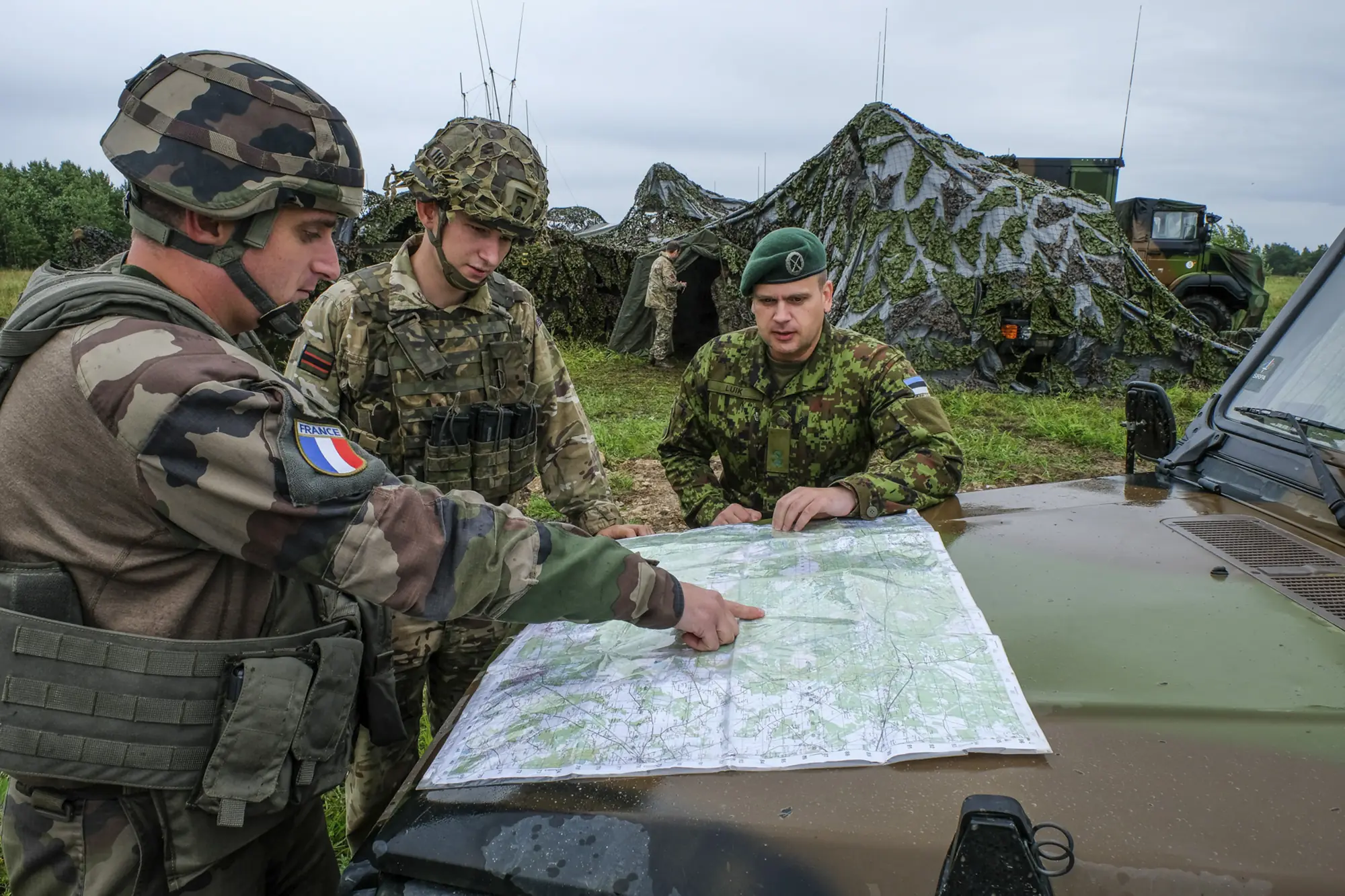 French, British and Estonian soldiers study a map together on a vehicle bonnet