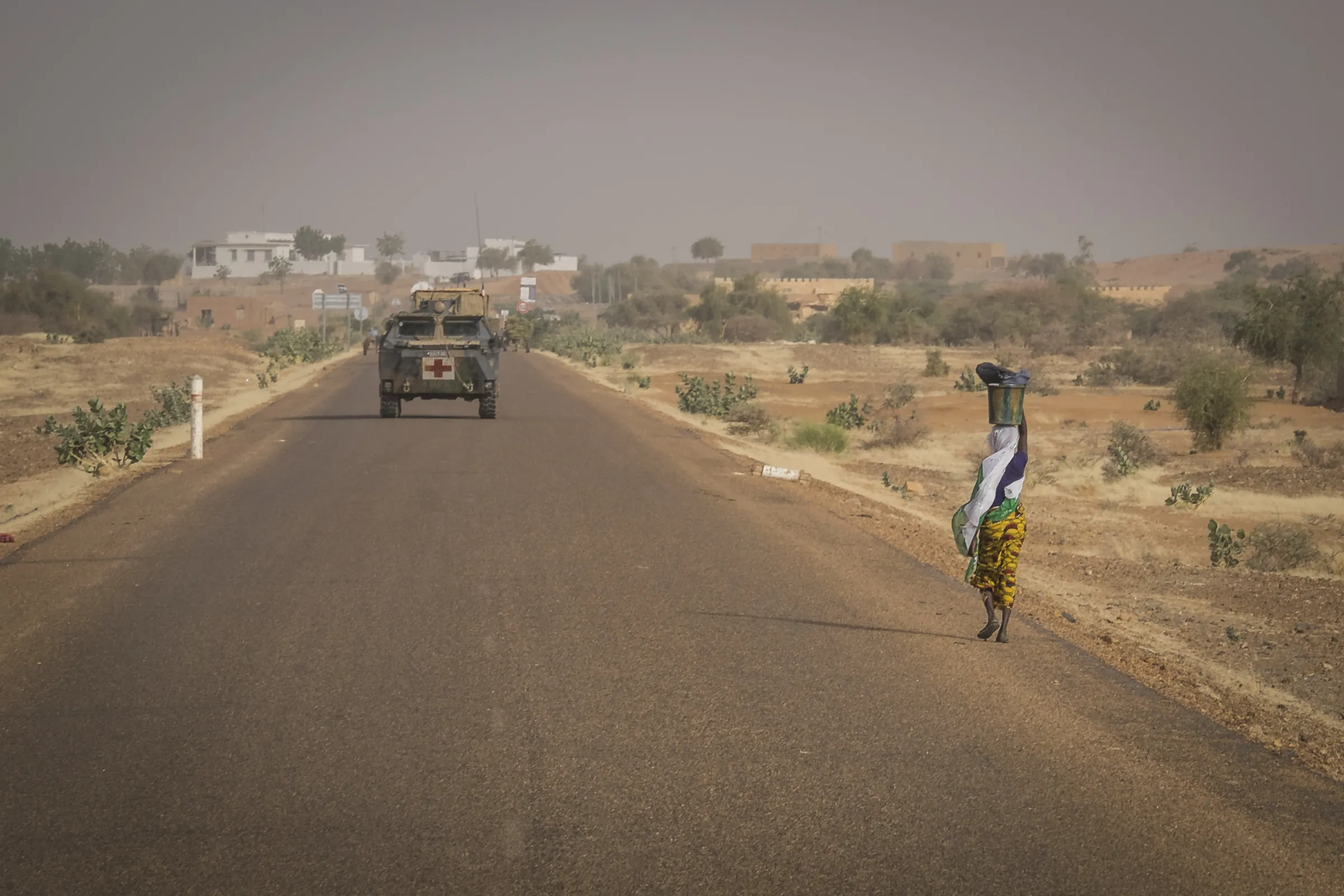 A French medical armoured vehicle on the road to Ansongo, Mali, as a woman passes carrying a bucket on her head