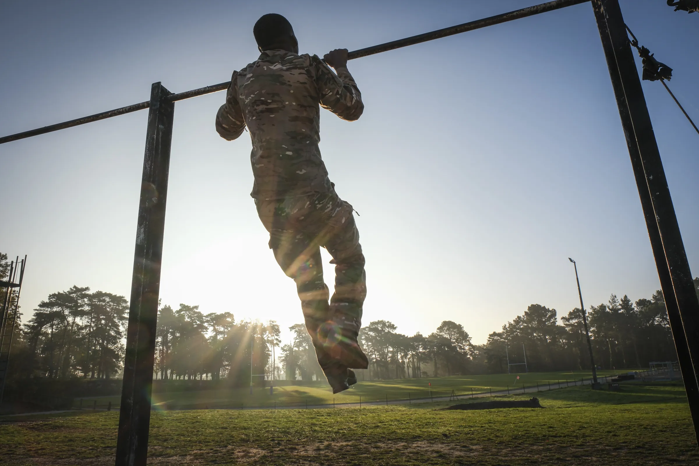 Silhouetted cadet doing pull-ups on outdoor bars against the low sun