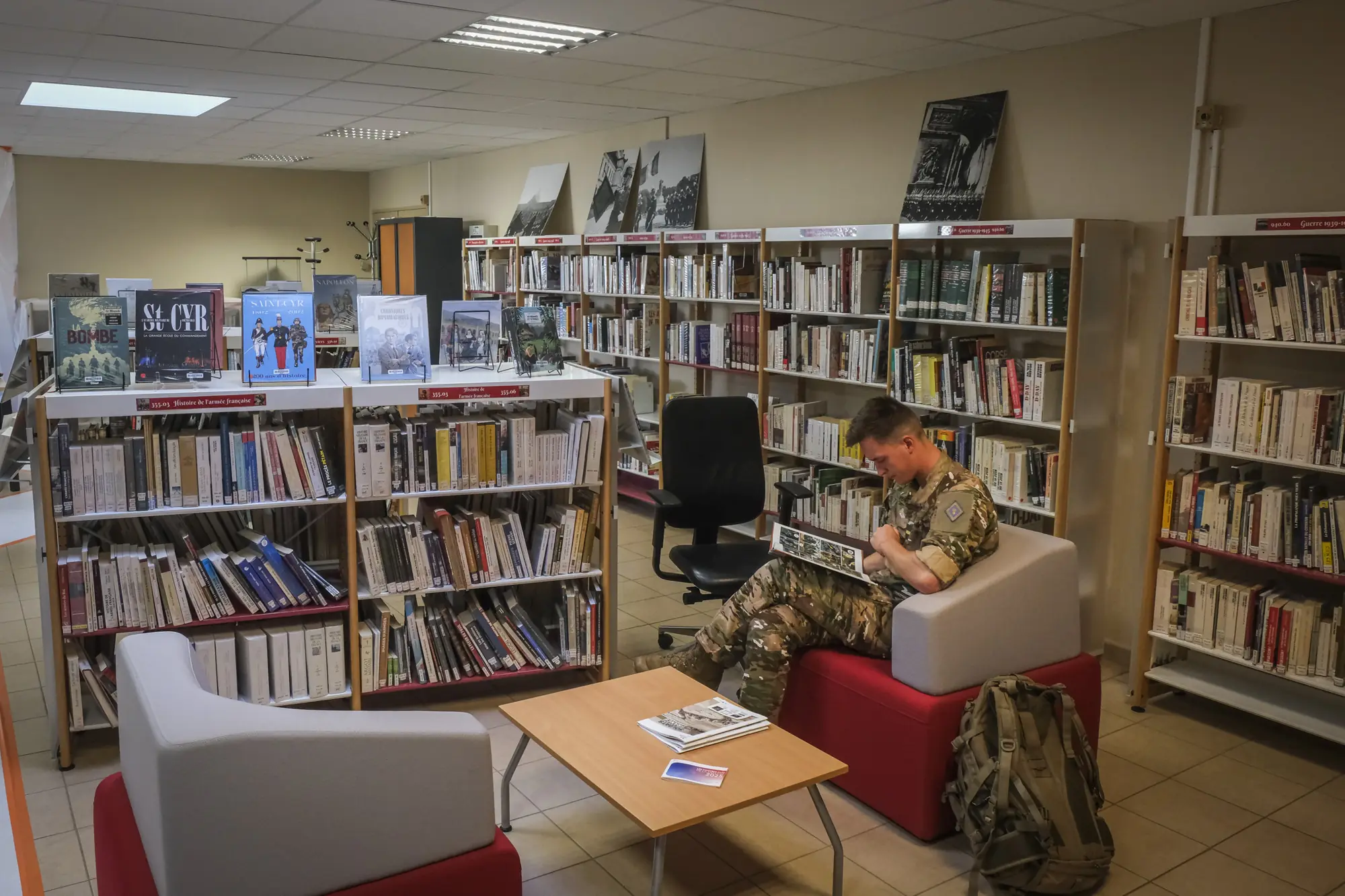 A cadet in field dress reads in the academy library, Saint-Cyr history books on the shelves