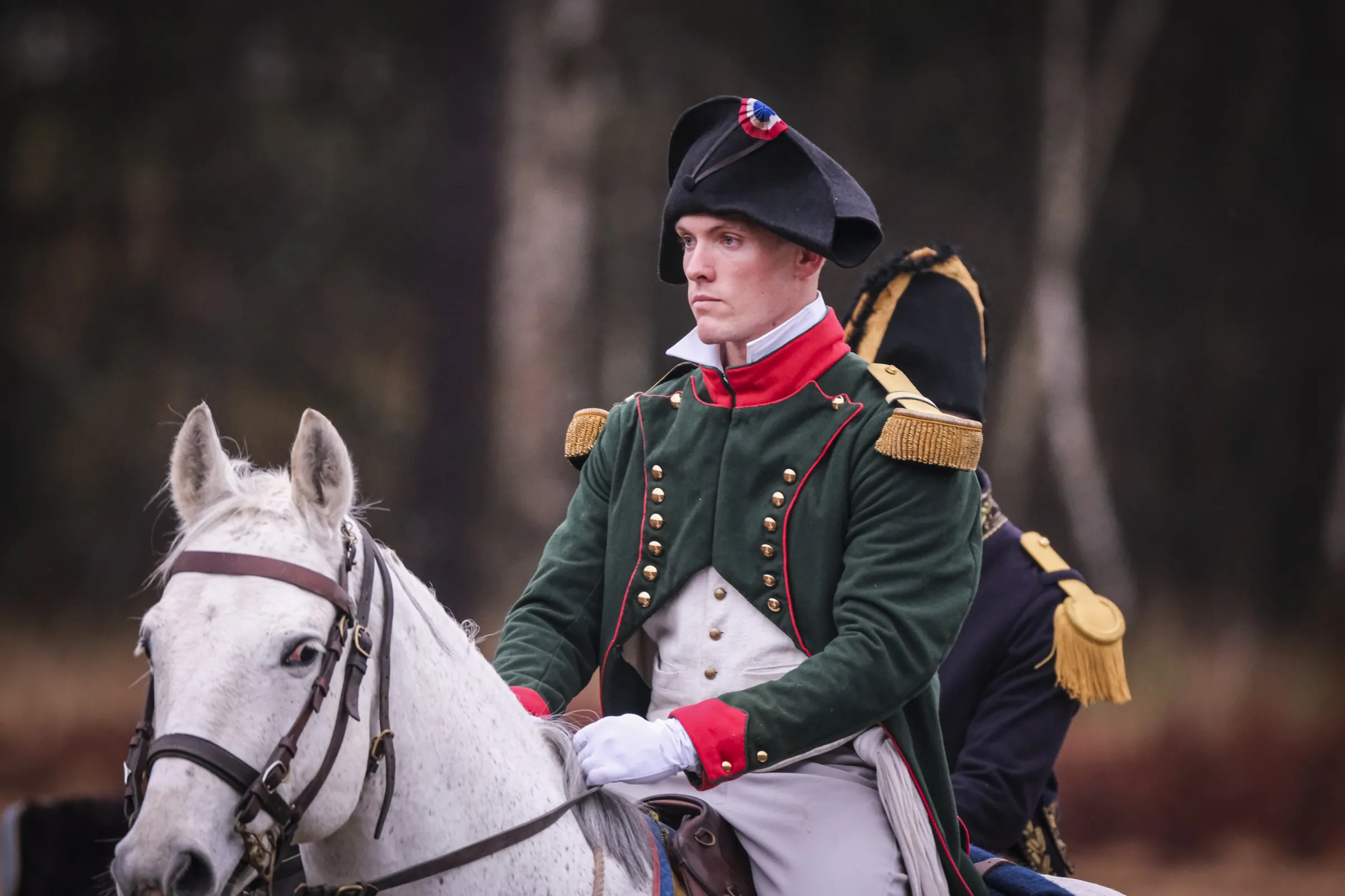 Close portrait of a cadet dressed as a Napoleonic officer in bicorne, astride a white horse
