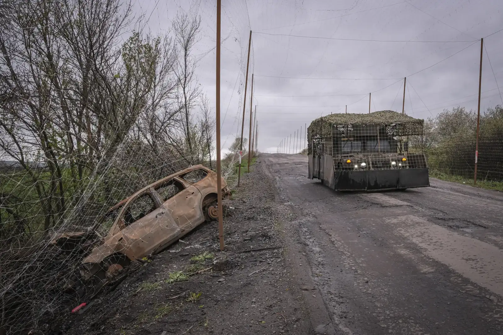 A burned-out civilian car under an anti-drone net corridor on a frontline road in eastern Ukraine