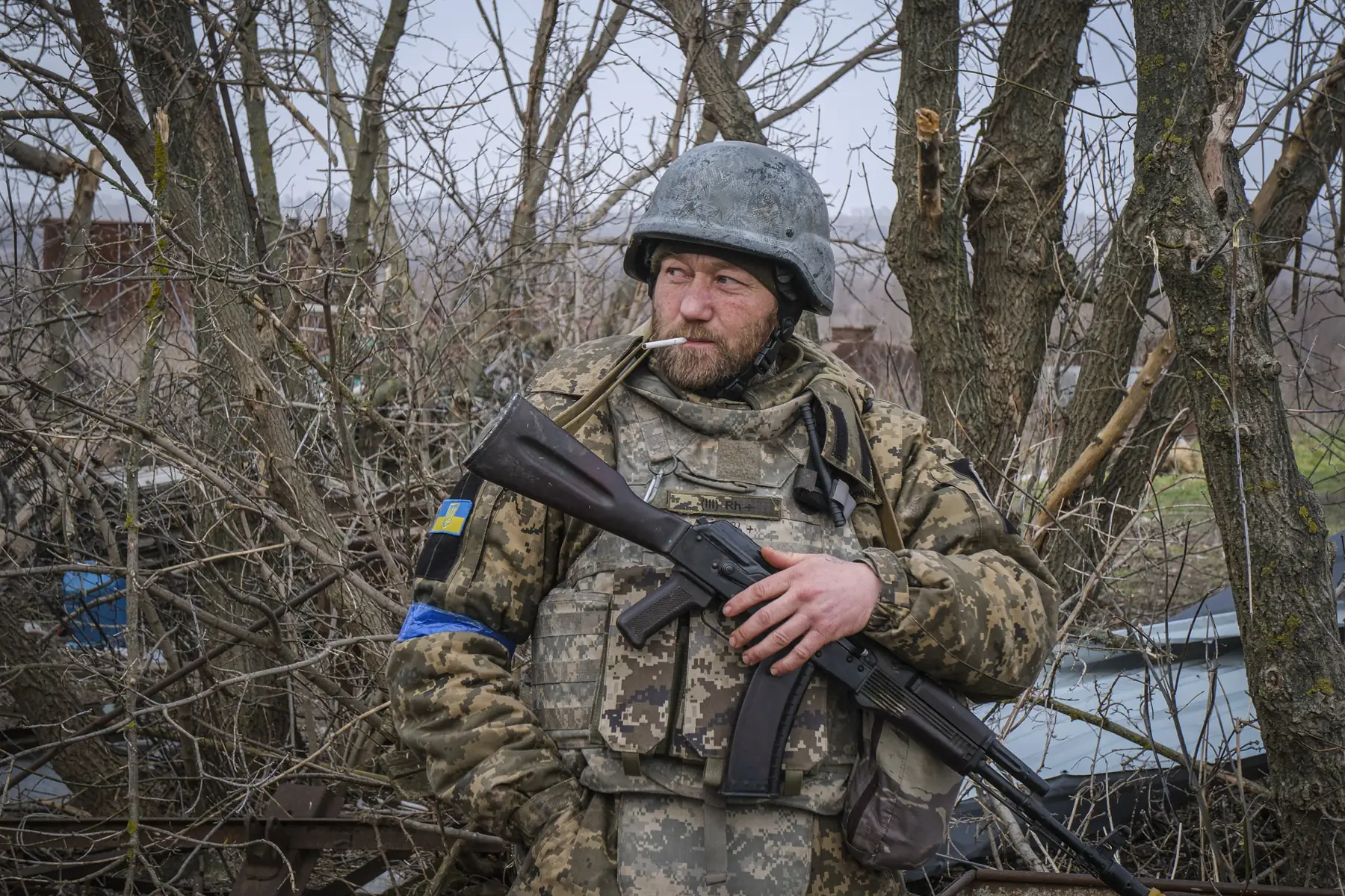 Portrait of a volunteer fighter with a cigarette, rifle and Ukrainian flag patch