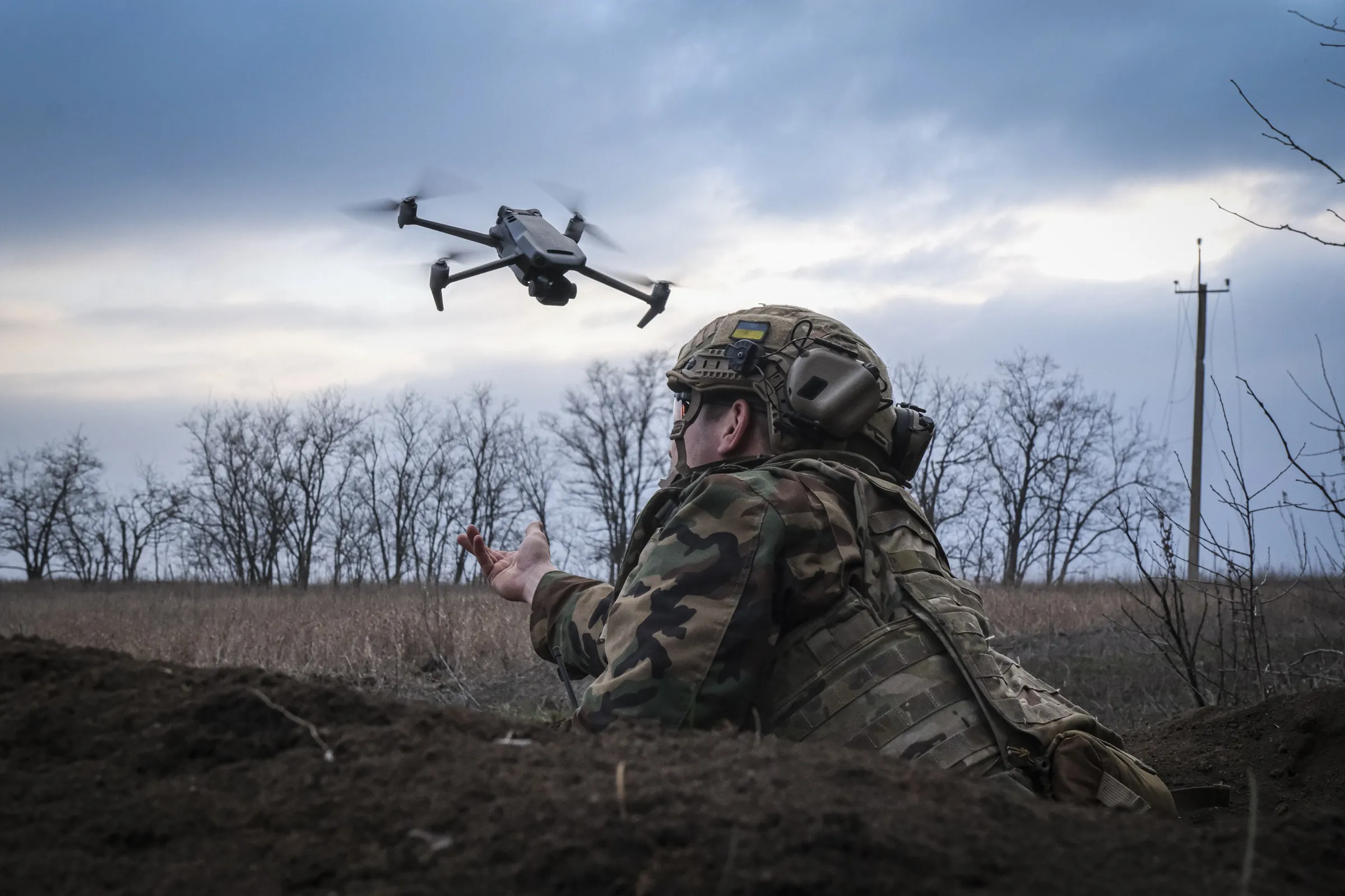 A Ukrainian soldier releases a small quadcopter drone from a trench at dusk
