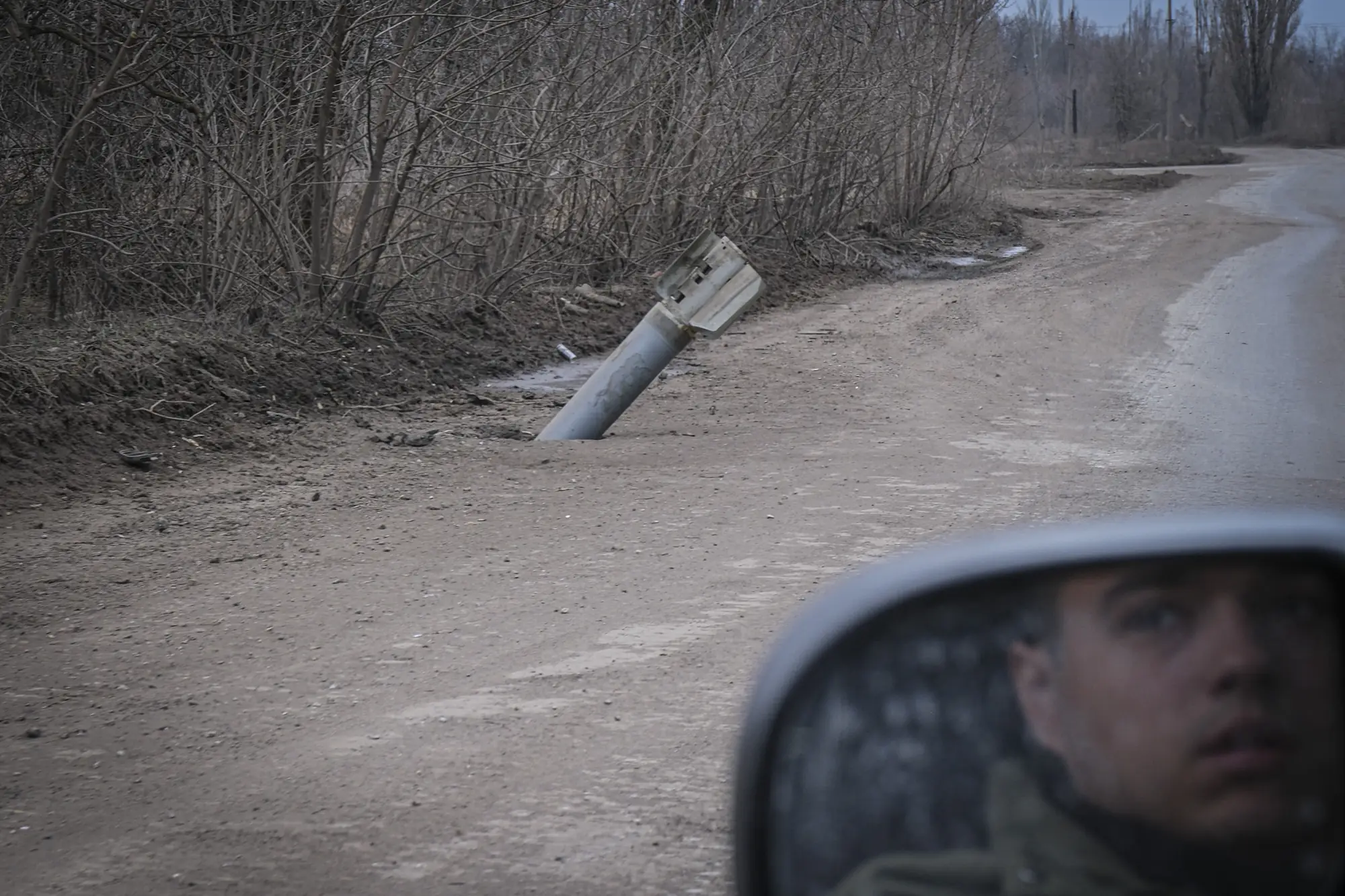 An unexploded Uragan rocket planted in the mud of a roadside in the Donbas, seen from a car mirror