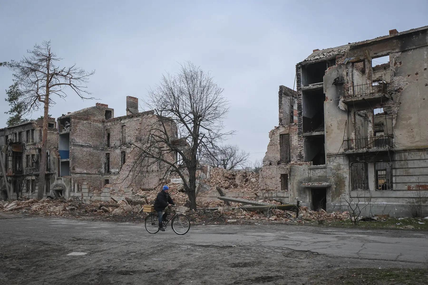 A man cycles past collapsed and burnt apartment blocks in a destroyed Ukrainian residential district