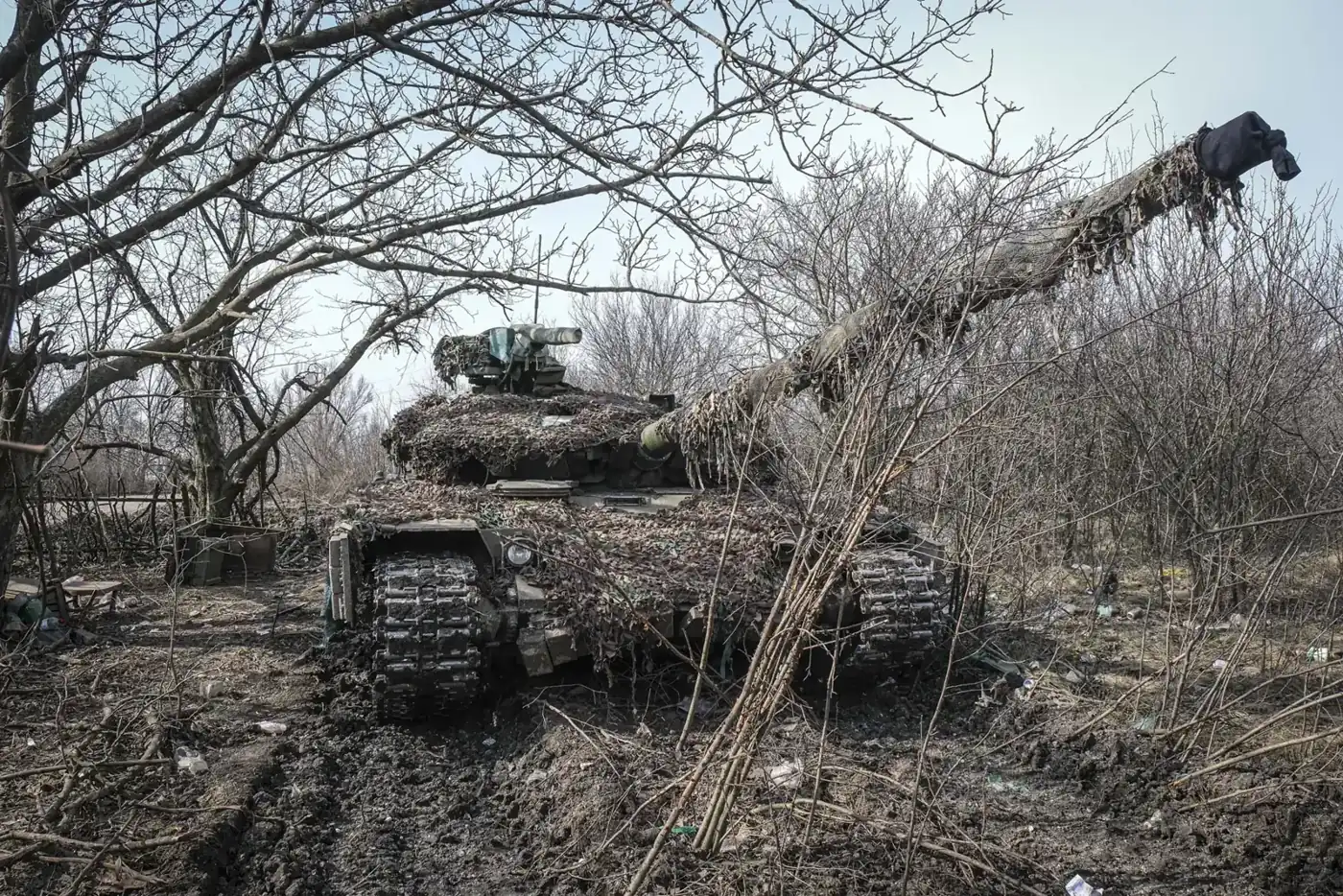 A T-64 tank hidden under camouflage netting in a leafless orchard