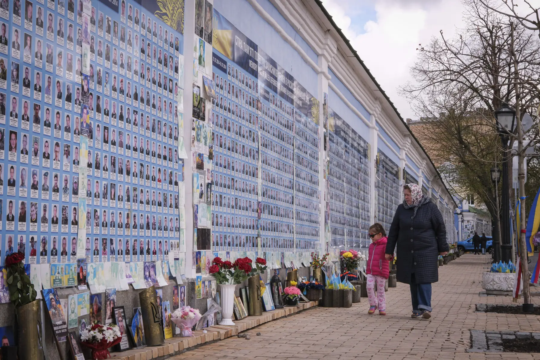 A grandmother and a little girl walk past the Wall of Remembrance of the Fallen at St Michael’s Monastery in Kyiv